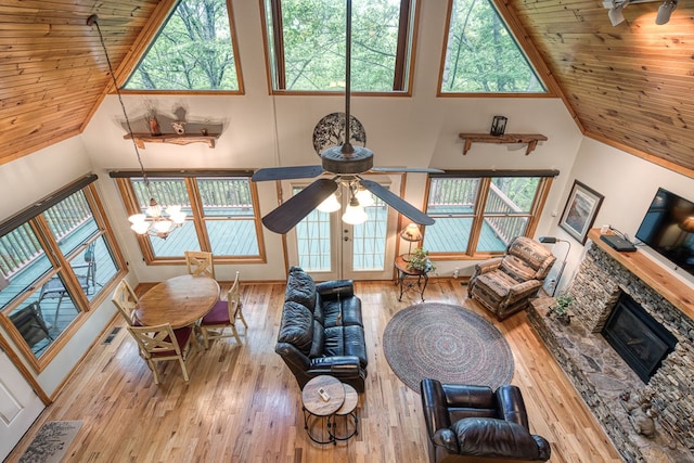 living room with healthy amount of natural light, hardwood / wood-style flooring, a stone fireplace, a ceiling fan, and high vaulted ceiling