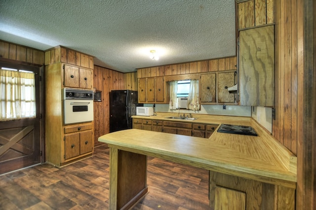 kitchen featuring a textured ceiling, black appliances, kitchen peninsula, and wooden walls