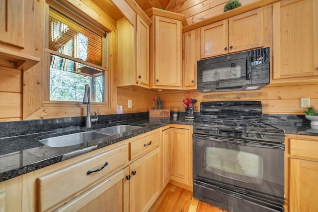 kitchen featuring light brown cabinets, dark stone countertops, light wood-type flooring, black appliances, and sink