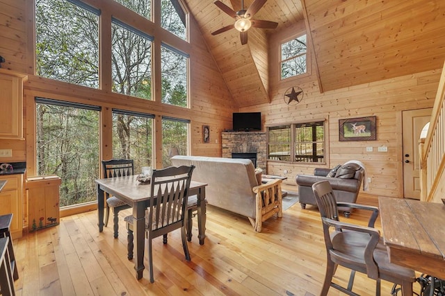 dining area featuring high vaulted ceiling, light hardwood / wood-style flooring, a fireplace, and ceiling fan