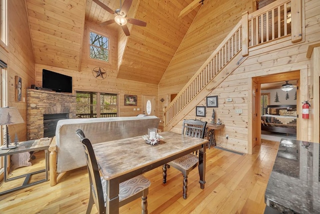 dining space featuring wooden ceiling, a stone fireplace, ceiling fan, light wood-type flooring, and high vaulted ceiling