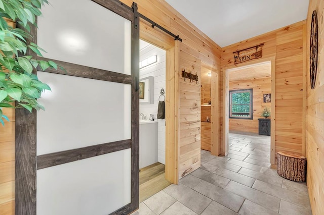 corridor with wooden walls, a barn door, and light tile flooring