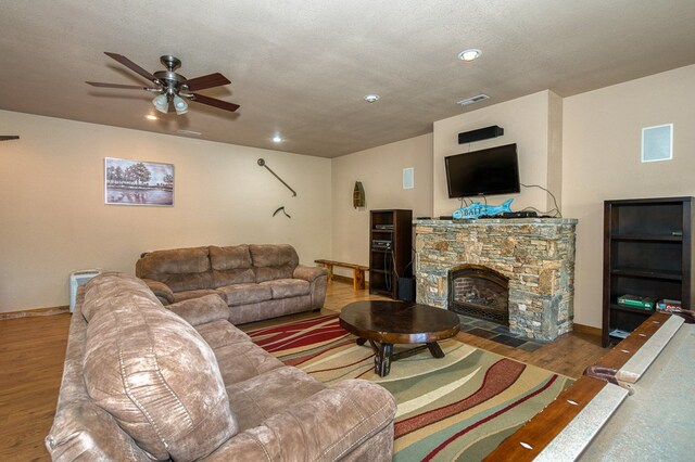living area with a stone fireplace, a ceiling fan, baseboards, wood finished floors, and visible vents