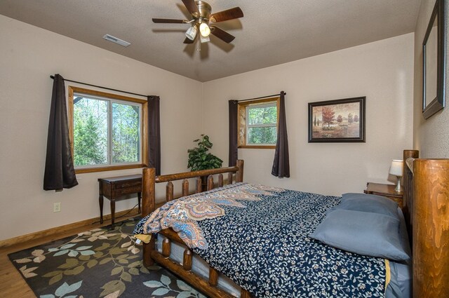 bedroom with baseboards, a ceiling fan, wood finished floors, and visible vents