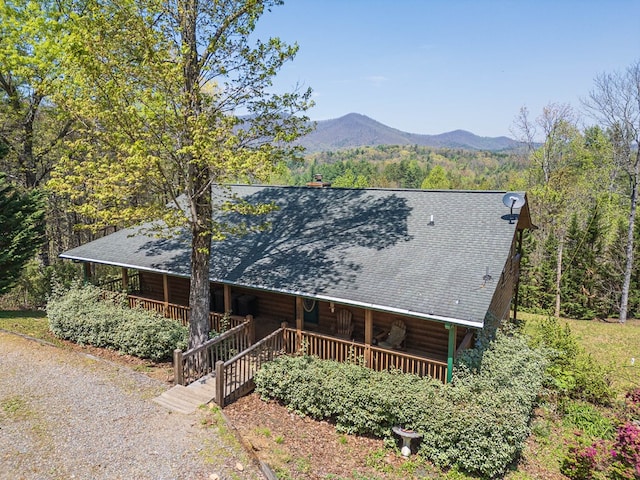 chalet / cabin featuring a porch, a forest view, a shingled roof, and a mountain view