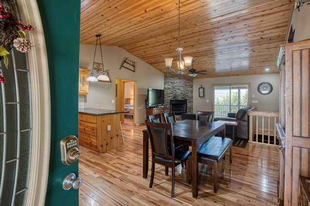 dining room with a fireplace, a ceiling fan, light wood-type flooring, vaulted ceiling, and wood ceiling