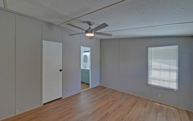 unfurnished bedroom with a decorative wall, a textured ceiling, wood finished floors, and ensuite bath