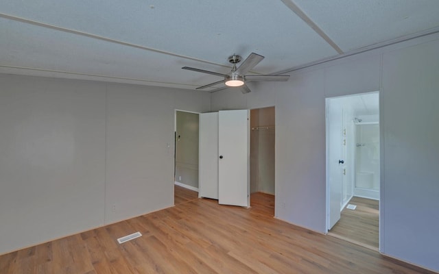 unfurnished bedroom featuring a ceiling fan, wood finished floors, ensuite bathroom, visible vents, and a closet