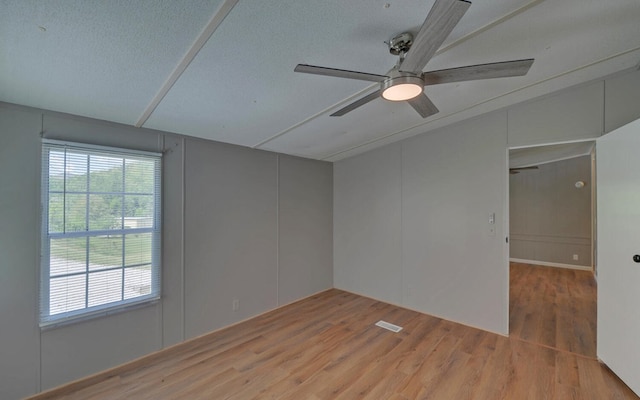 unfurnished room featuring a ceiling fan, a decorative wall, wood finished floors, and vaulted ceiling
