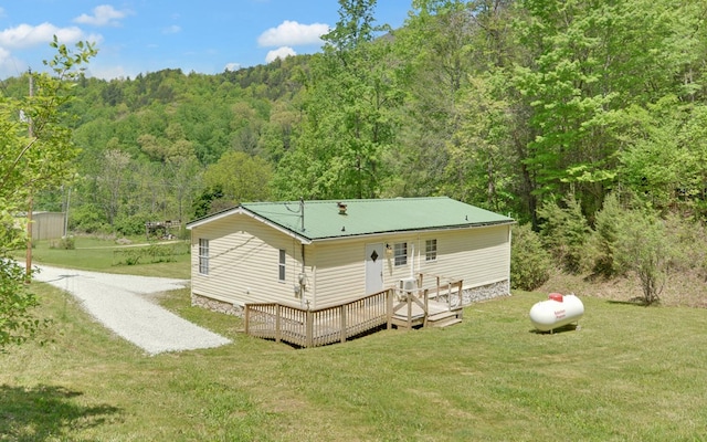 back of property featuring a wooden deck, a yard, metal roof, and a forest view