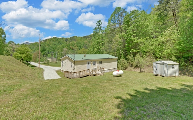 rear view of property featuring a deck, a storage unit, a lawn, an outbuilding, and a wooded view