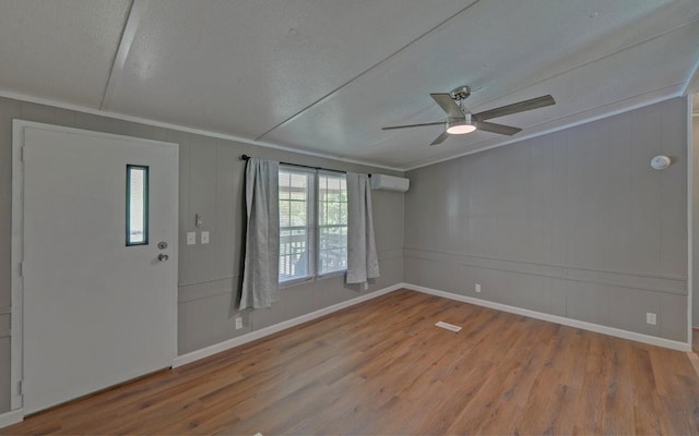 interior space with a decorative wall, a wall unit AC, a ceiling fan, and wood finished floors
