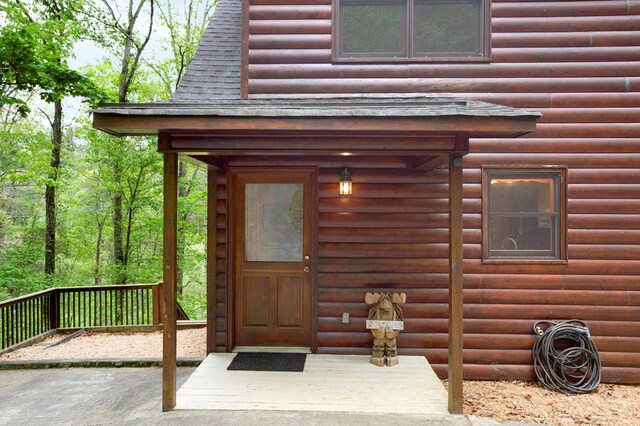 entrance to property featuring roof with shingles and faux log siding