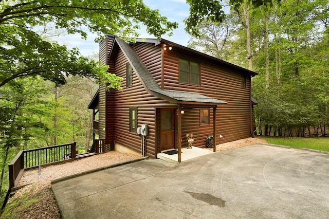 view of front of home featuring roof with shingles, faux log siding, a chimney, and a patio area