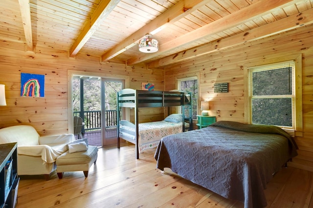 bedroom featuring light wood finished floors, beam ceiling, wooden walls, and access to exterior