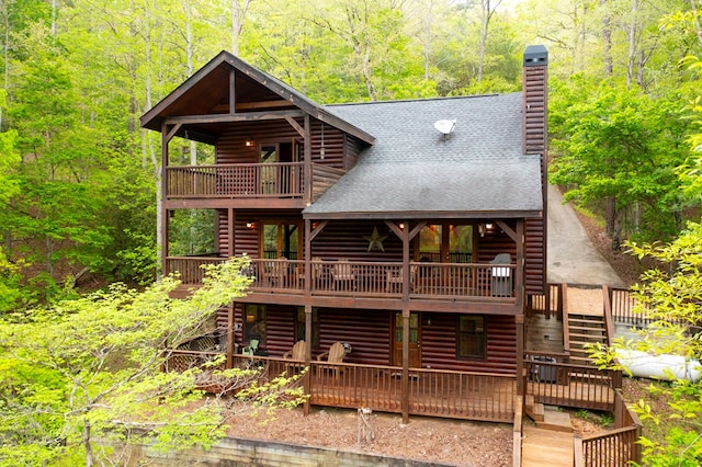 back of property featuring stairway, a deck, a chimney, and roof with shingles