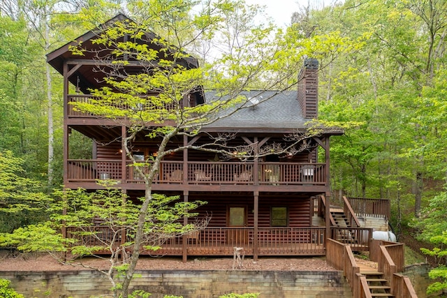 rear view of house featuring a deck, faux log siding, a chimney, stairs, and a forest view