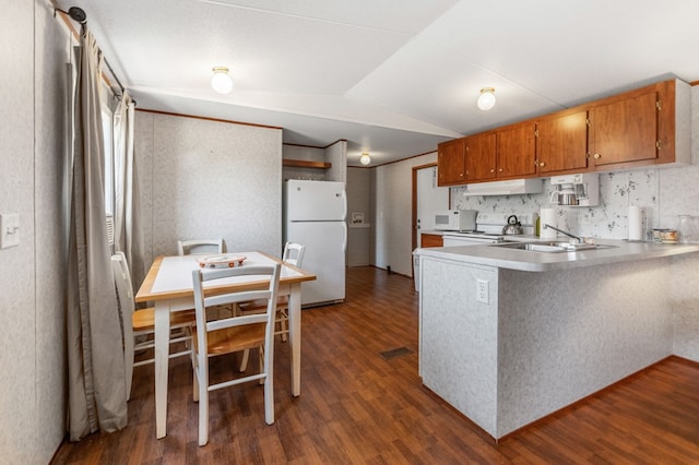 kitchen with kitchen peninsula, dark wood-type flooring, white appliances, lofted ceiling, and sink