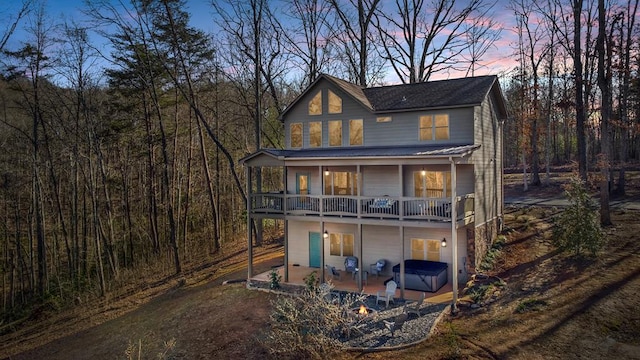 back house at dusk with a balcony, a patio, and a hot tub