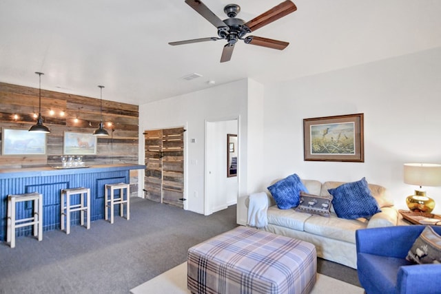 living room with dark colored carpet, ceiling fan, and wood walls