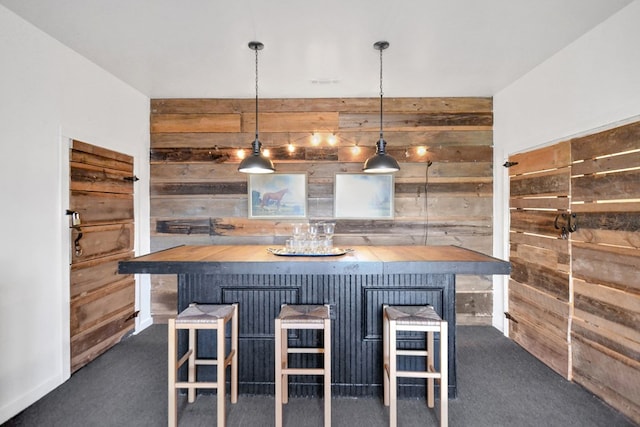 kitchen with a breakfast bar, wood walls, dark colored carpet, butcher block countertops, and decorative light fixtures