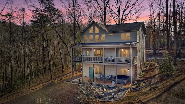 back house at dusk with a balcony, a hot tub, and a patio area