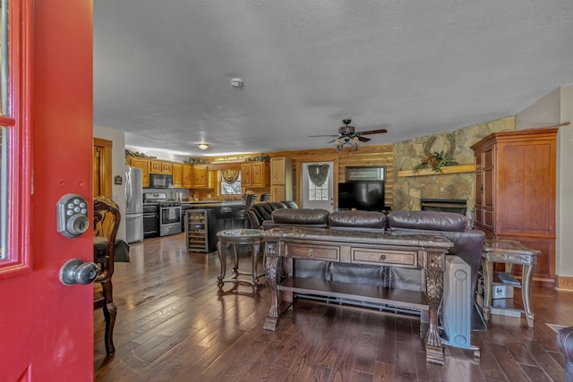 living room with wine cooler, a stone fireplace, a textured ceiling, dark hardwood / wood-style flooring, and ceiling fan