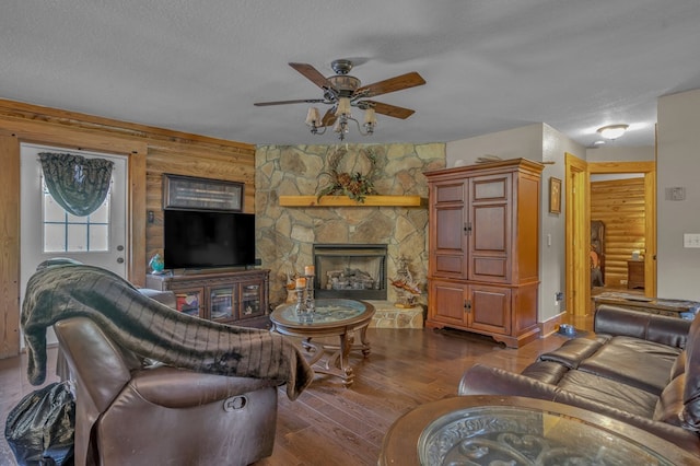 living room featuring dark wood-type flooring, ceiling fan, a fireplace, and a textured ceiling