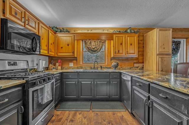 kitchen featuring hardwood / wood-style flooring, stainless steel appliances, a textured ceiling, and dark stone counters