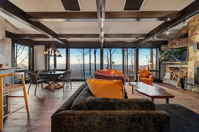 sunroom / solarium with a notable chandelier, visible vents, rail lighting, a stone fireplace, and beamed ceiling