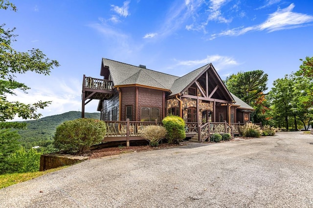 view of front of property with a shingled roof, stone siding, a mountain view, and a balcony