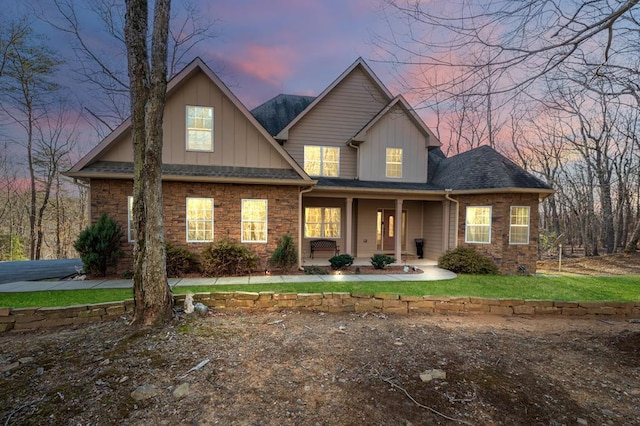 view of front of property with stone siding, roof with shingles, covered porch, a front lawn, and board and batten siding