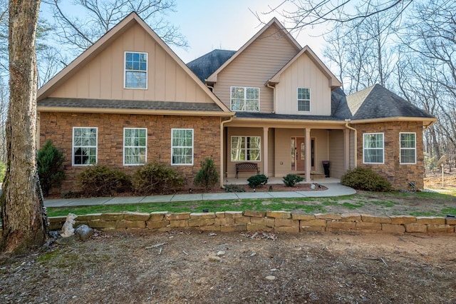 view of front of home with covered porch, roof with shingles, board and batten siding, and stone siding