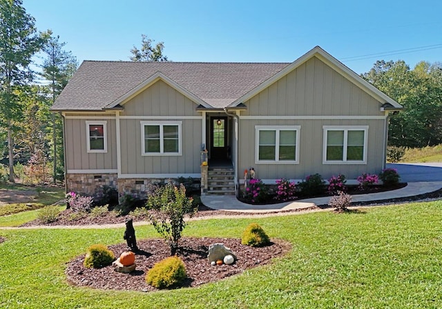 view of front of home featuring stone siding, a front lawn, board and batten siding, and a shingled roof