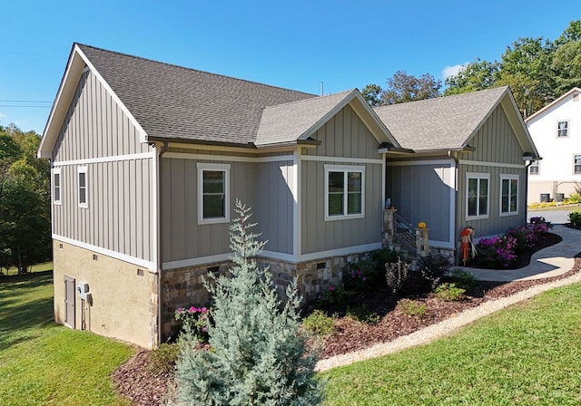 view of front of property featuring stone siding, a front lawn, board and batten siding, and roof with shingles