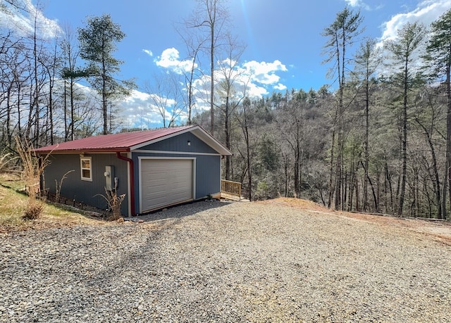 detached garage with gravel driveway and a wooded view