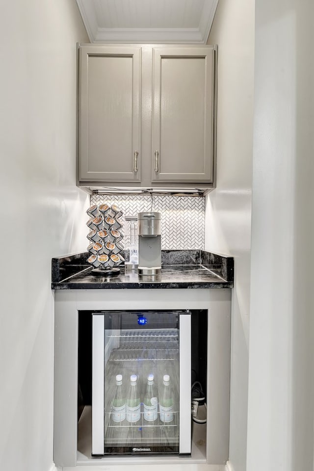 bar with decorative backsplash, beverage cooler, ornamental molding, and dark stone countertops