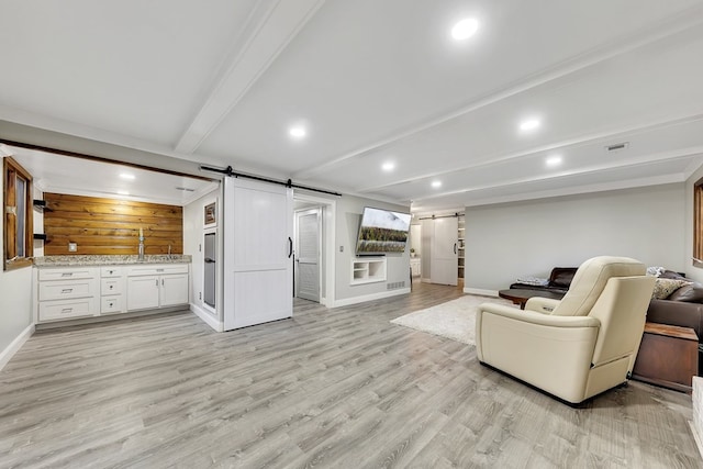 living room featuring light hardwood / wood-style flooring, beam ceiling, and a barn door