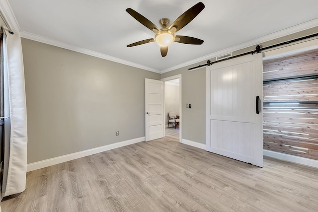 unfurnished bedroom featuring ceiling fan, ornamental molding, a barn door, and light hardwood / wood-style flooring