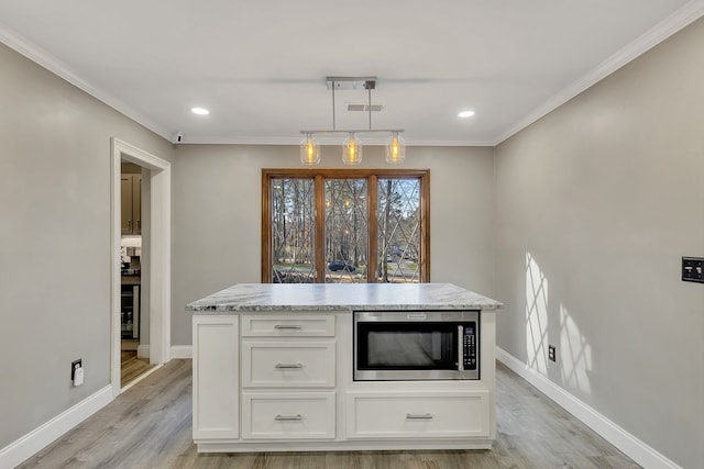 kitchen featuring stainless steel microwave, decorative light fixtures, crown molding, and white cabinetry