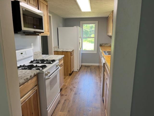 kitchen with white appliances, light wood-type flooring, and sink