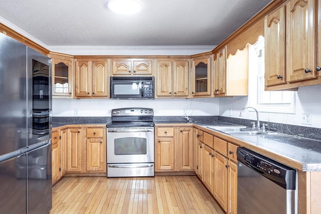 kitchen with appliances with stainless steel finishes, sink, light wood-type flooring, ornamental molding, and a textured ceiling