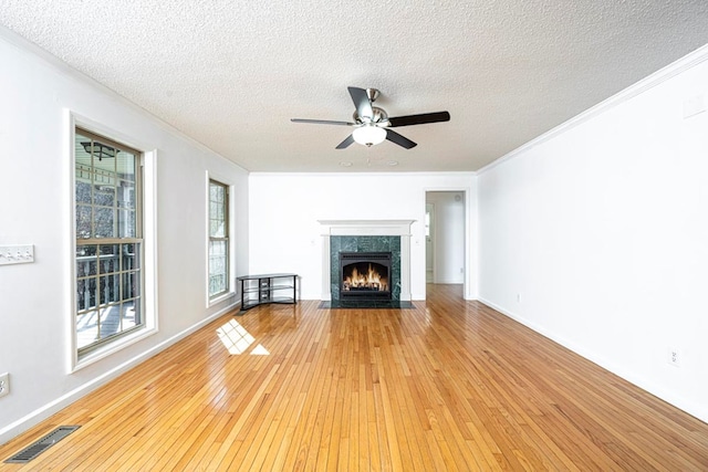 unfurnished living room with a tile fireplace, ceiling fan, wood-type flooring, ornamental molding, and a textured ceiling