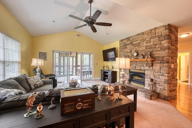 living room with vaulted ceiling, a fireplace, a textured ceiling, ceiling fan, and light hardwood / wood-style flooring