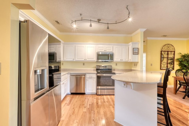 kitchen with appliances with stainless steel finishes, light hardwood / wood-style floors, a breakfast bar area, and white cabinets