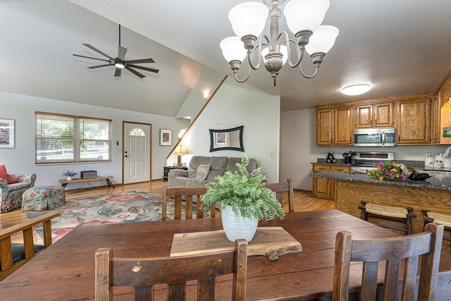 dining space featuring ceiling fan with notable chandelier, light wood-style flooring, a textured ceiling, and vaulted ceiling