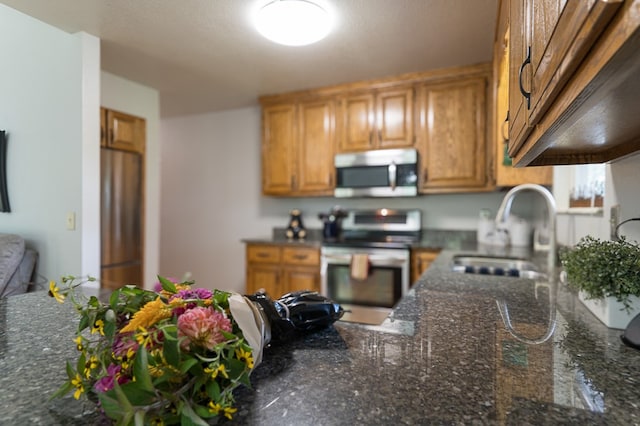 kitchen with dark stone countertops, brown cabinets, appliances with stainless steel finishes, and a sink