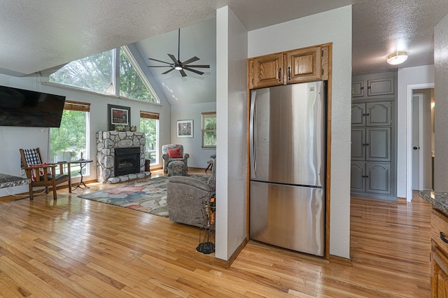 kitchen with a stone fireplace, light wood-style flooring, freestanding refrigerator, and a ceiling fan