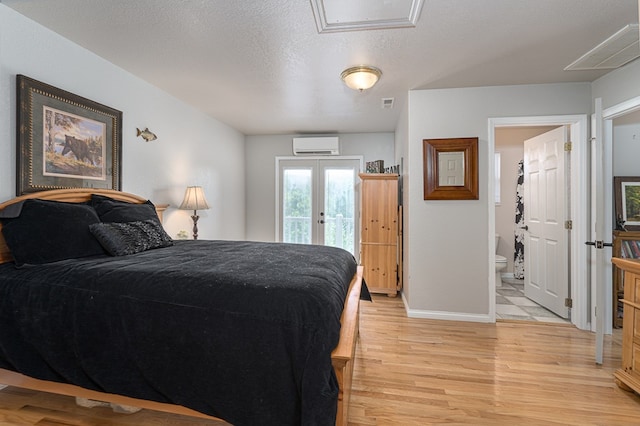 bedroom featuring connected bathroom, an AC wall unit, light wood-style flooring, french doors, and access to outside