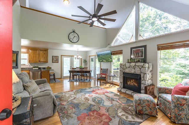 living area featuring a fireplace, a high ceiling, ceiling fan with notable chandelier, and light wood finished floors